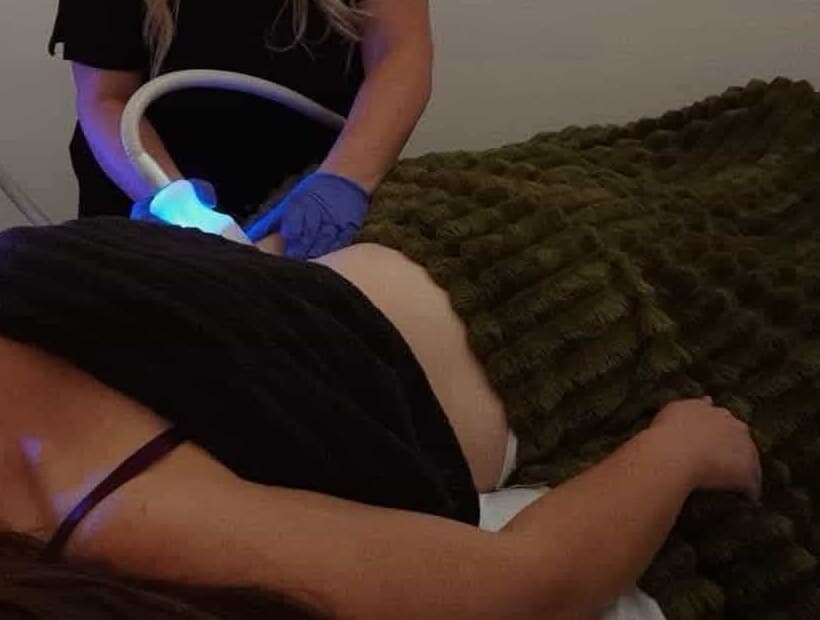 Anonymous body sculpting treatment detail with handheld applicator and warm clinical setup.