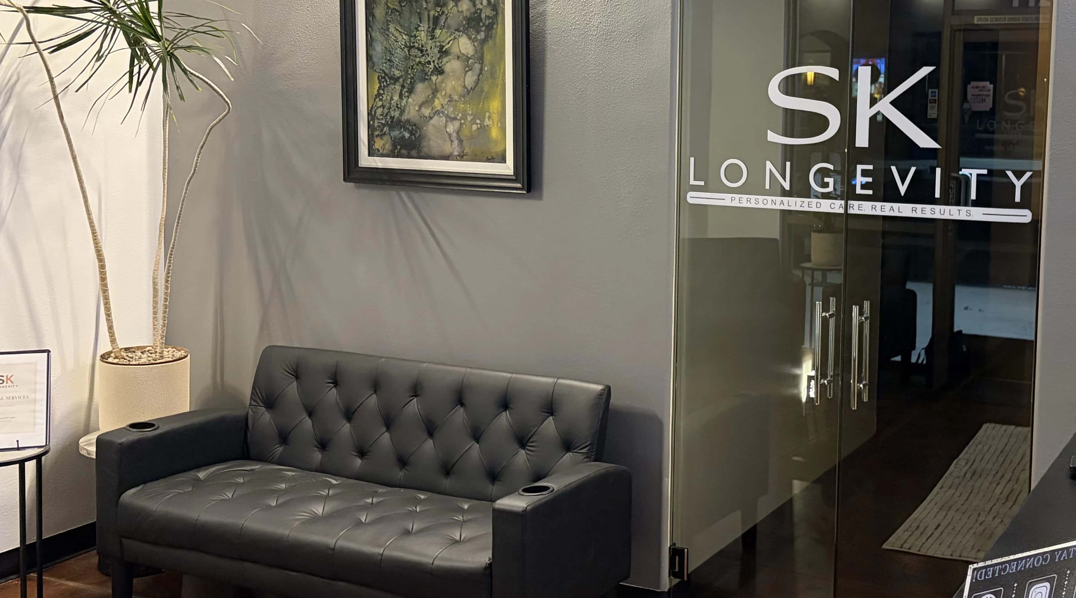 An SK Longevity waiting area with seating, framed artwork, and the etched glass entry door.